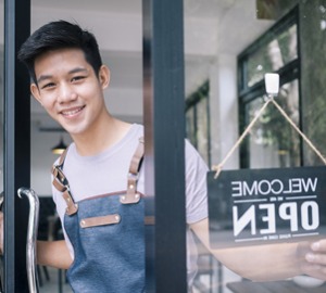 Young businessman wearing an apron turning the Welcome/Open sign on the door