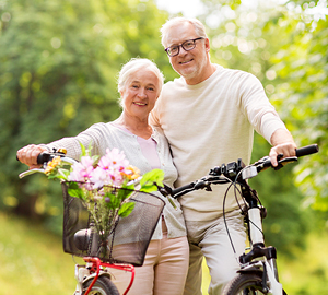Older couple out in nature smiling while riding their bikes.