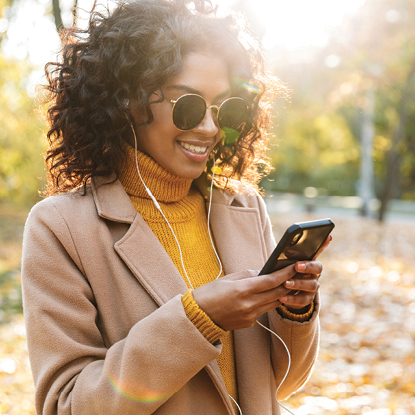 Black woman wearing sunglasses and smiling while holding her cell phone outdoors.