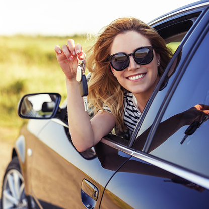 Young woman sitting in her car smiling while holding keys to her new car.